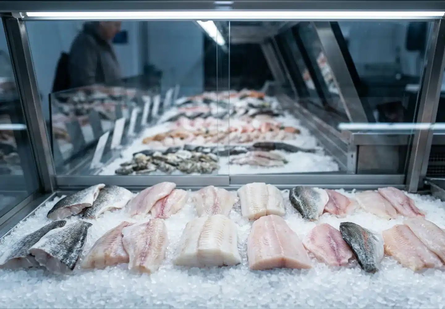 Fish fillets on ice behind glass at a retail counter with a small unreadable card propped among them, the display that prompts the question of why buy frozen fish